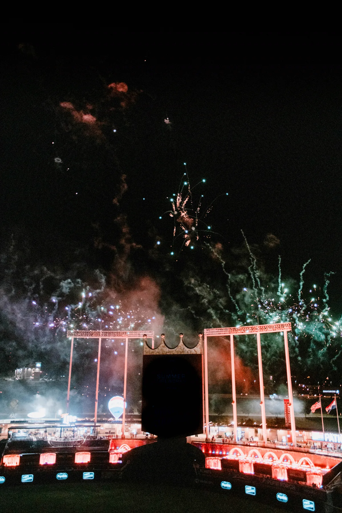 Arrowhead Stadium entrance gate lit up at night with red and green fireworks bursting in the sky above the scoreboard