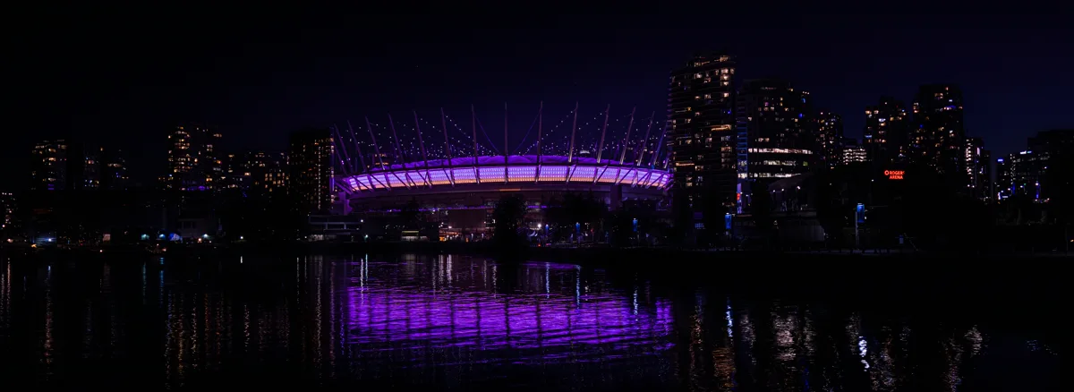 BC Place retractable dome glowing purple at night with its reflection shimmering in False Creek, Vancouver's downtown skyline behind it