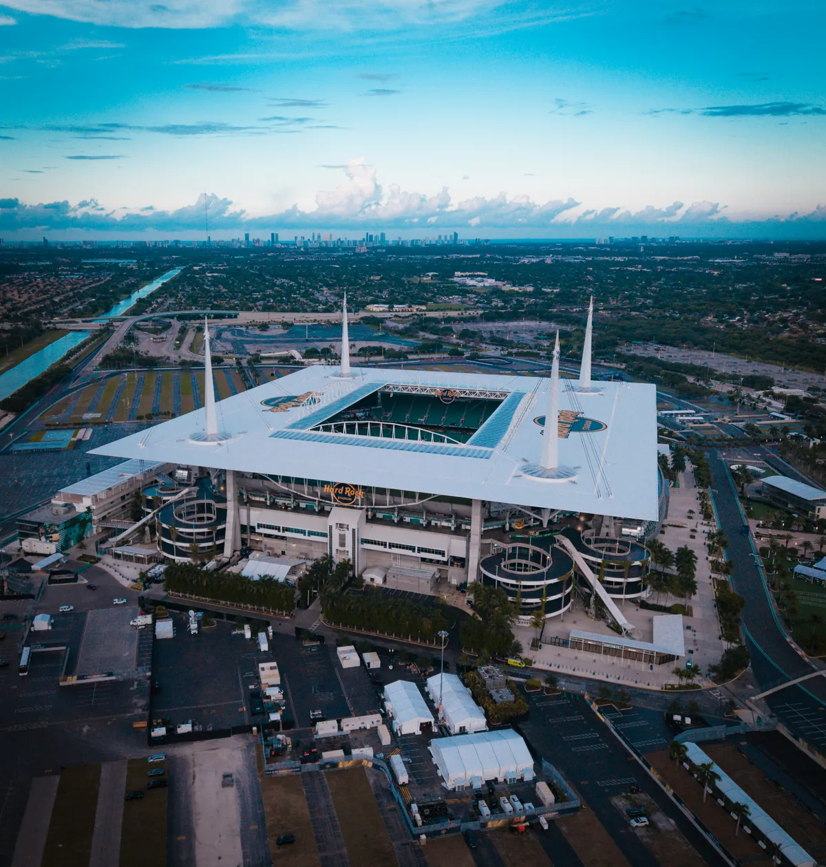 Hard Rock Stadium aerial view showing its distinctive white canopy roof and corner spires with the Miami skyline on the horizon