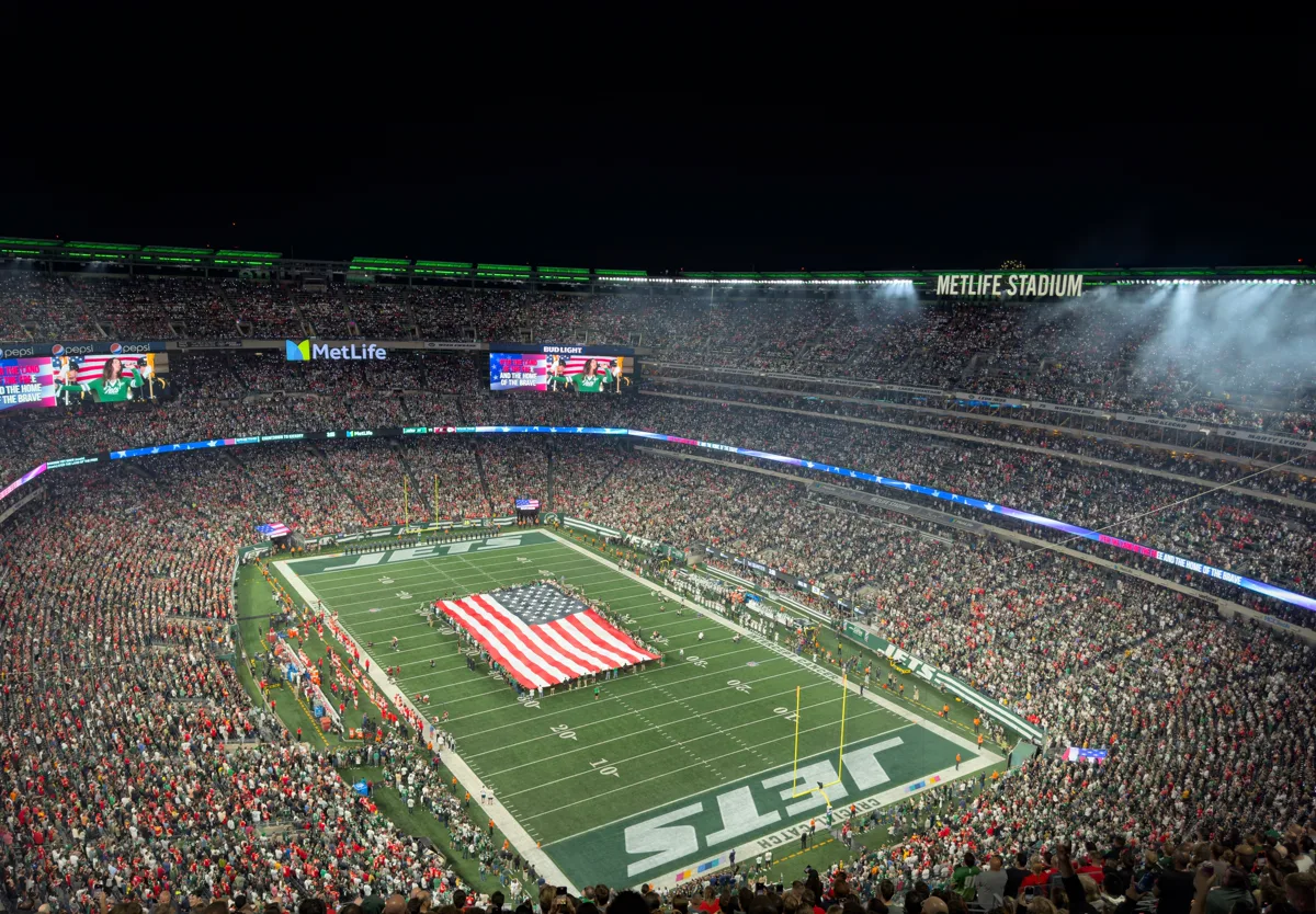 MetLife Stadium packed interior at night with a giant American flag covering the entire field at a sold-out event
