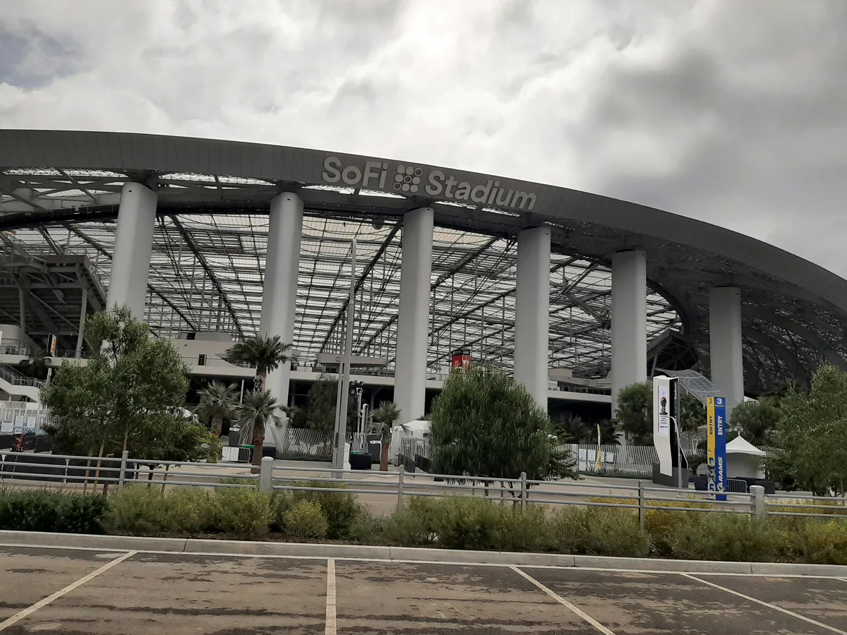 SoFi Stadium exterior showing the sweeping curved roof and glass façade with palm trees lining the entrance in Inglewood